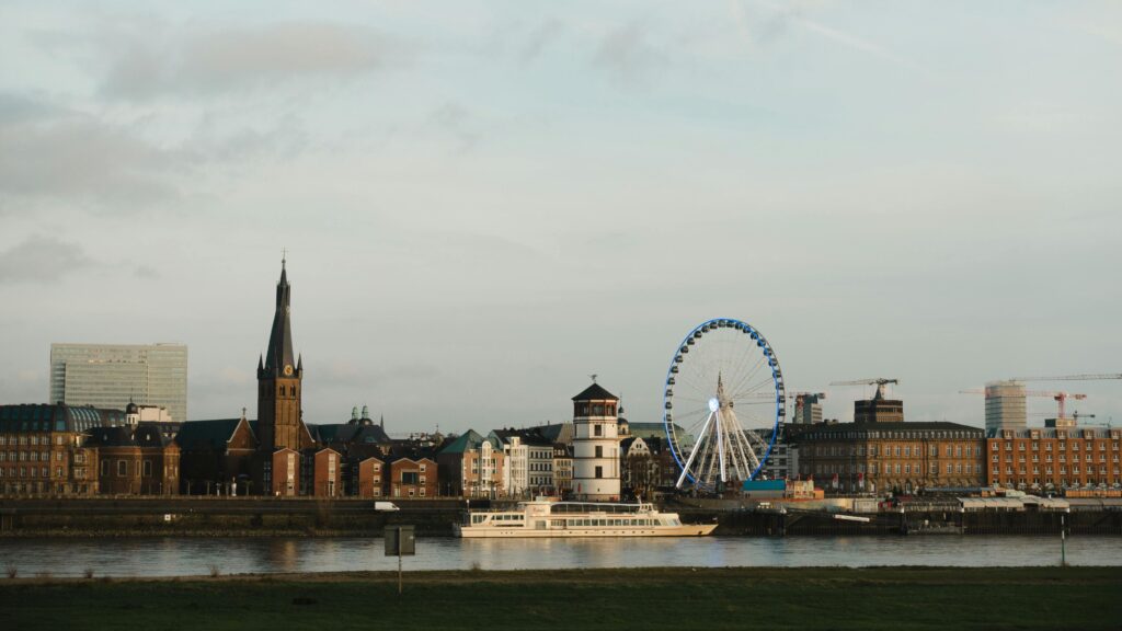 Picturesque view of Düsseldorf with a ferris wheel by the river and historic buildings.