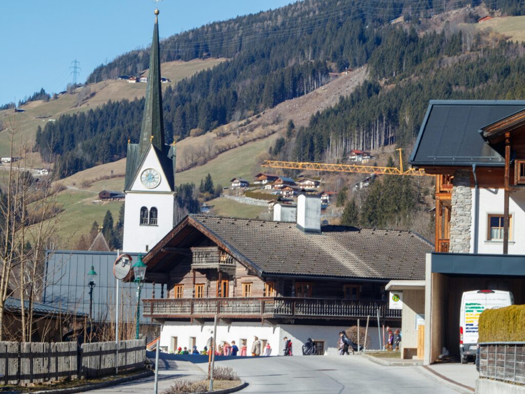 Picturesque view of an Alpine village with a church steeple and scenic mountain backdrop.