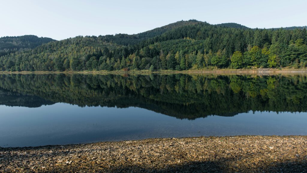 Tranquil reflection of forested hills in a calm lake in Langelsheim, Germany. A perfect escape to nature.